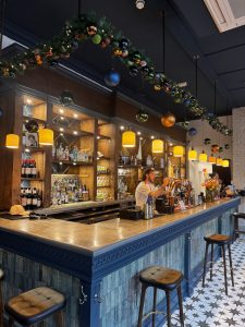 Christmas styling in a stylish bar, featuring lush festive garlands of greenery and baubles suspended above a blue bar with brass detailing