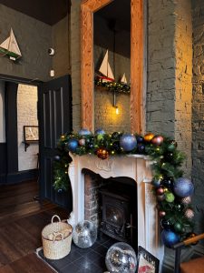 A fireplace dressed with lush evergreen garlands, colourful baubles and oversized silver ornaments